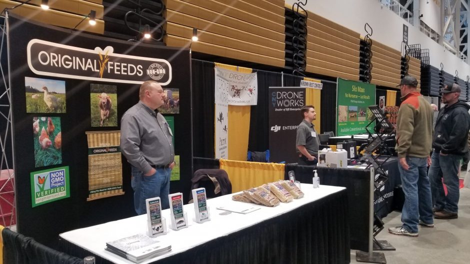 A farm show vendor with the name "organic seeds." To the left of the vendor is a seperate vendor who is showcasing drones.
