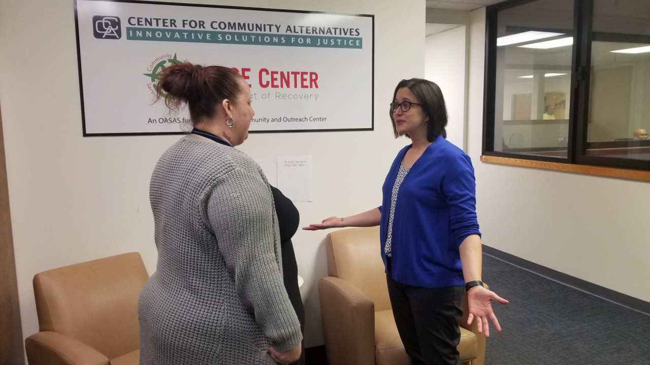Two women have a conversation in front of a sign that reads "Center For Community Alternatives."