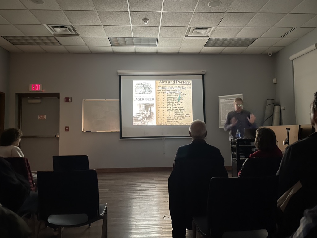 A dark room is illuminated by a presentation about the history of beer in Syracuse.