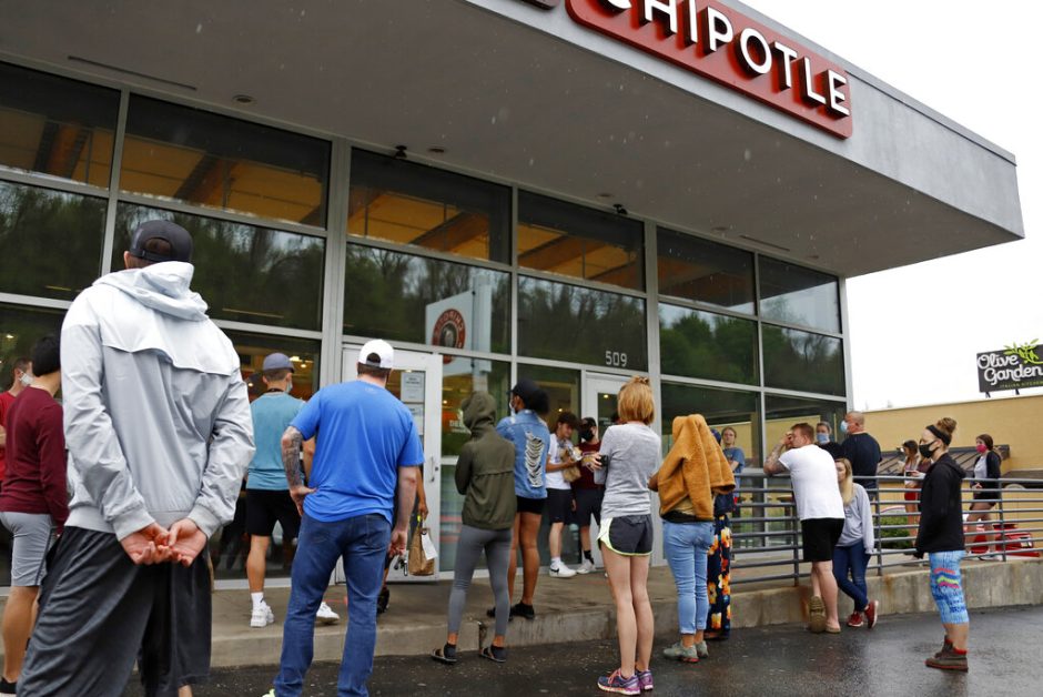 A crowd waits outside a Chipotle restaurant.