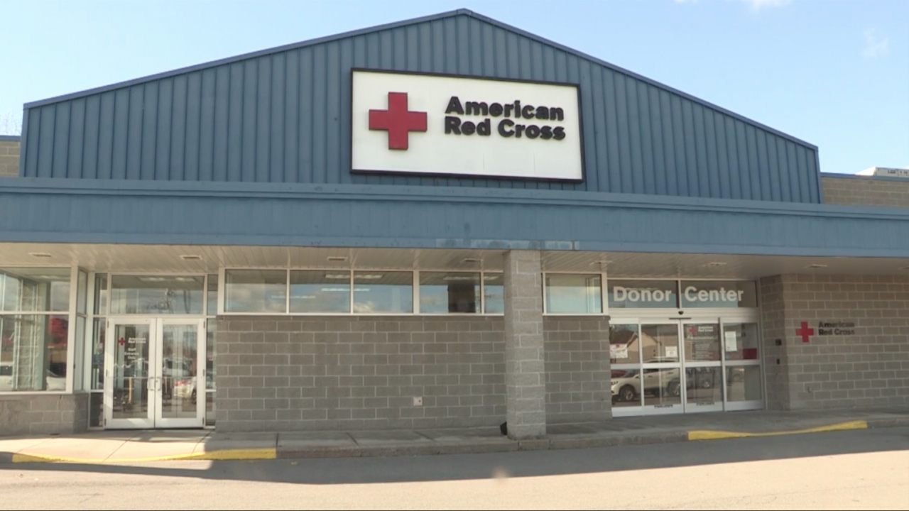 The exterior of the Liverpool blood donation is grey stone on the bottom and blue siding on the top. There is a large, white sign on top with the American Red Cross logo.