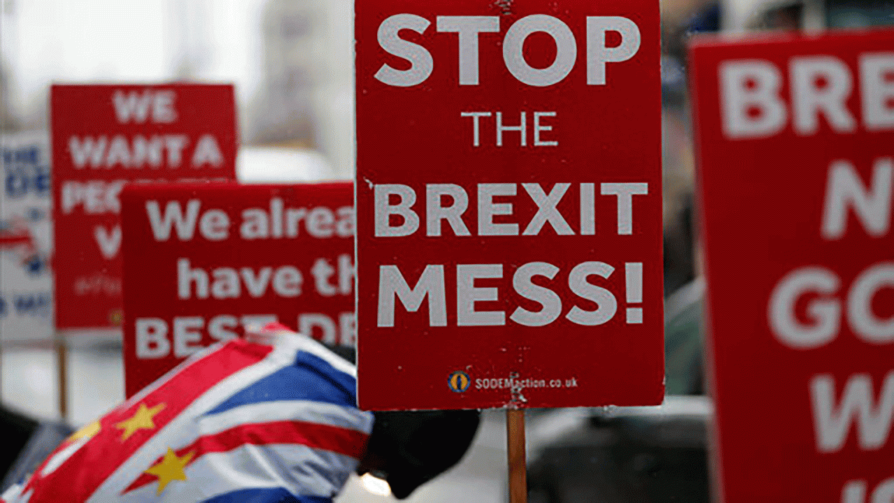 Protesters hold several signs criticizing the current Brexit situation with slogans such as "Stop the Brexit Mess!"