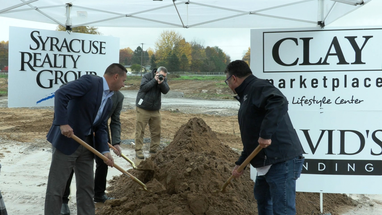 People put shovels into a mound of dirt at the Clay Marketplace groundbreaking ceremony.