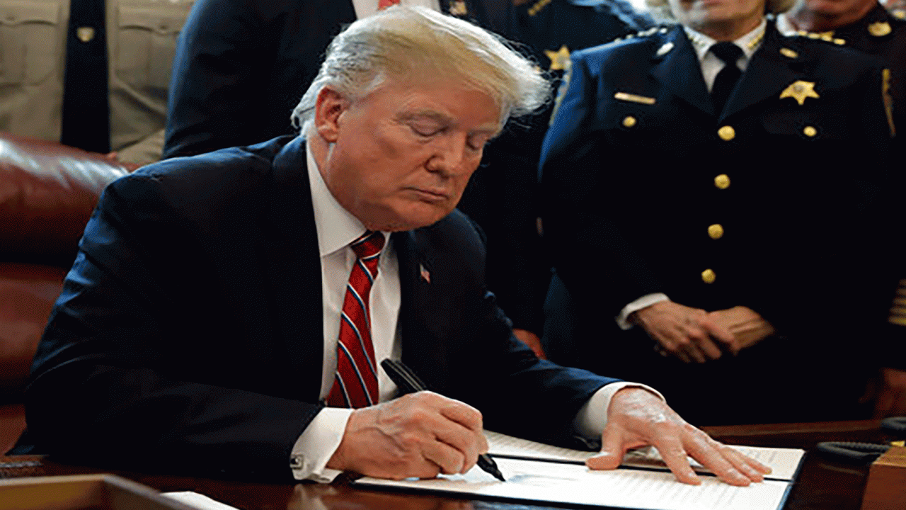 President Donald Trump signs his first veto while sitting at a desk surrounded by administration officials