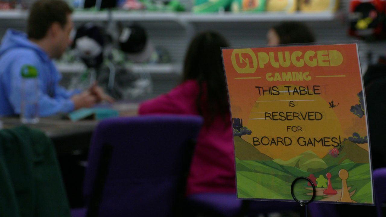 A paper sign depicting the Unplugged Gaming logo with shelves in the back.