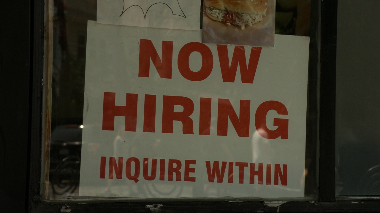 A white sign with the words "Now Hiring, Inquire Within" printed in red letters.