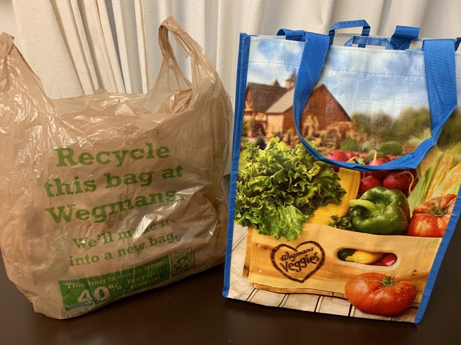 A Wegmans plastic bag next to a reusable bag.