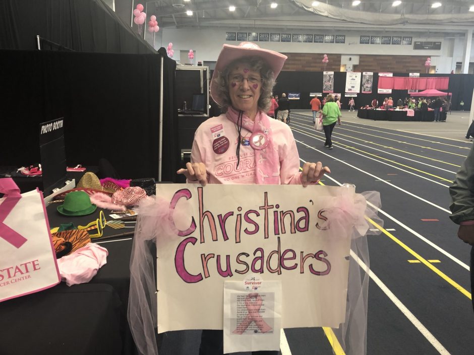 Breast cancer survivor poses with her decorated sign that says "Christina's Crusaders"