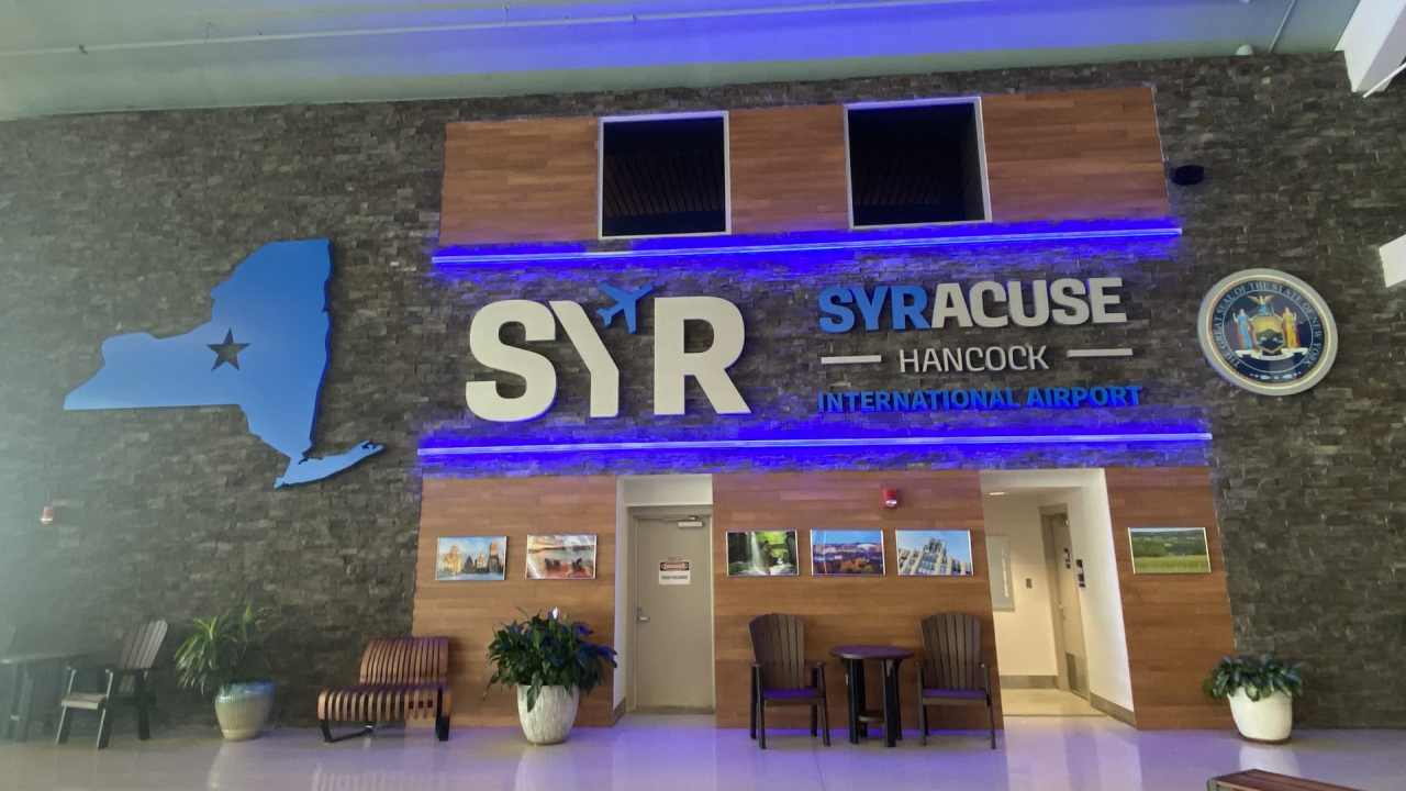 Syracuse Hancock International Airport sign on wall, next to Blue outline of New York State