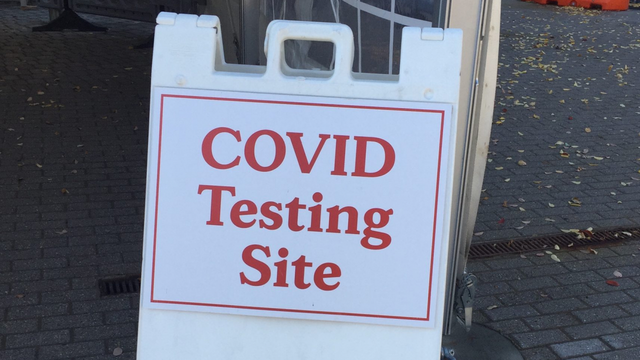 White sign with orange lettering that reads "COVID Testing Site"