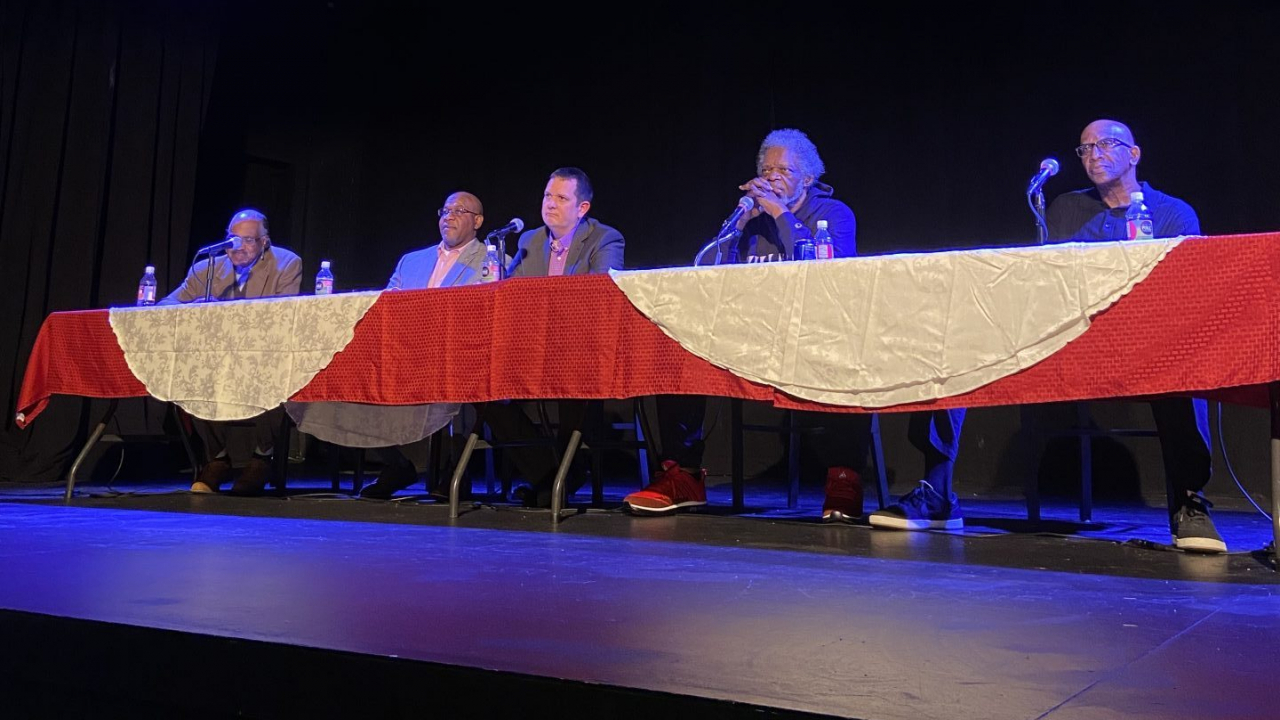 Men sitting at a table on a stage.