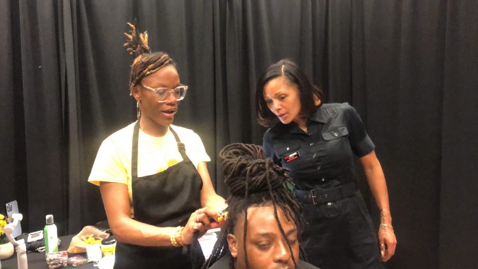 A hairstylist observing another hairstylist retesting the locs on a client