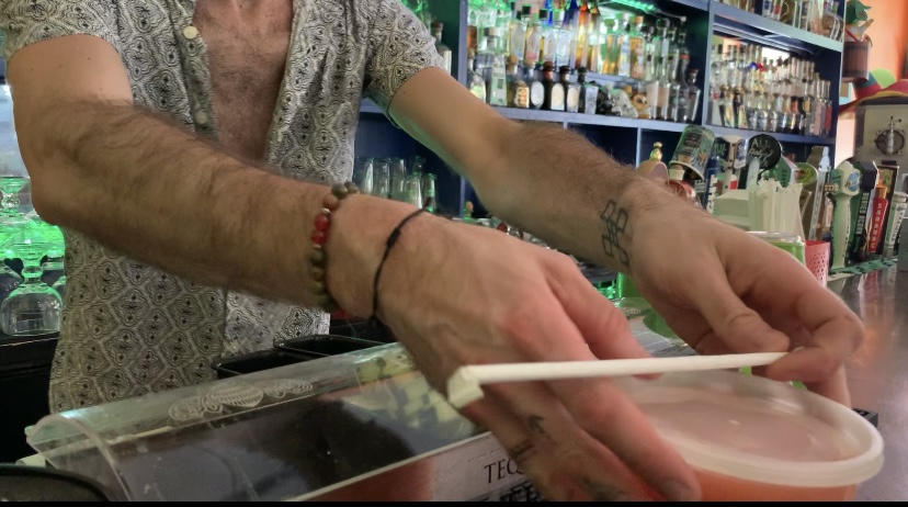 Hands placing a to-go cocktail on the bar with an unopened straw on top.