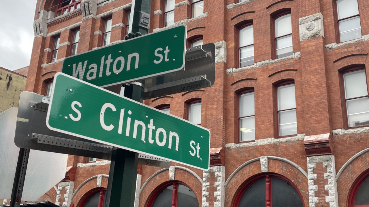 Two street signs that read "Clinton Street" and "Walton Street" stand in front of a brick building.