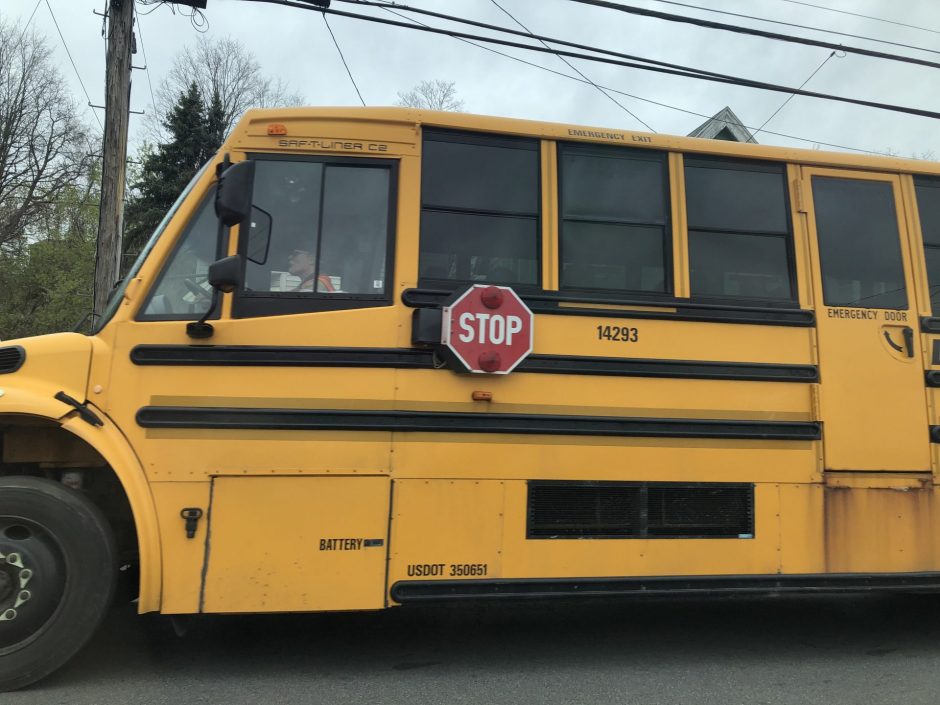 Side of yellow school bus on the street driving students home from school.