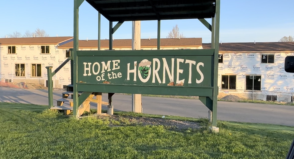 "Home of the Hornets" painted on a green, wooden scorer's box at a soccer field.