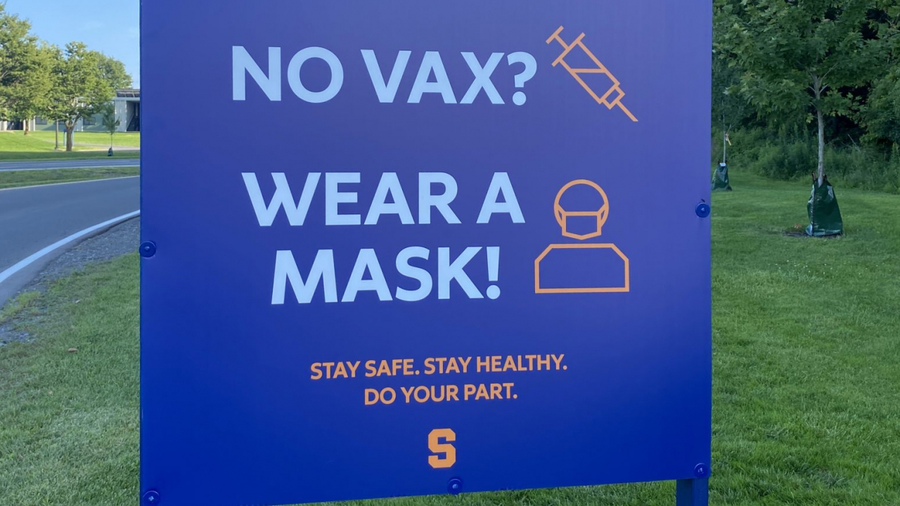 Blue sign with orange writing telling unvaccinated people to wear a mask.