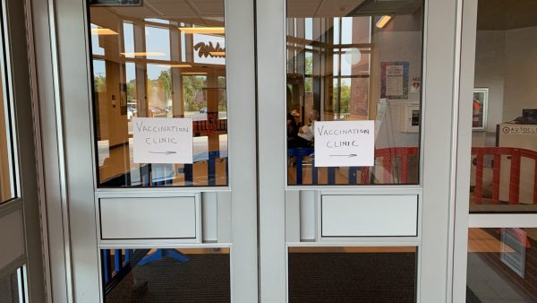 "Vaccine Clinic" written on white paper with a right arrow is posted on two glass doors.