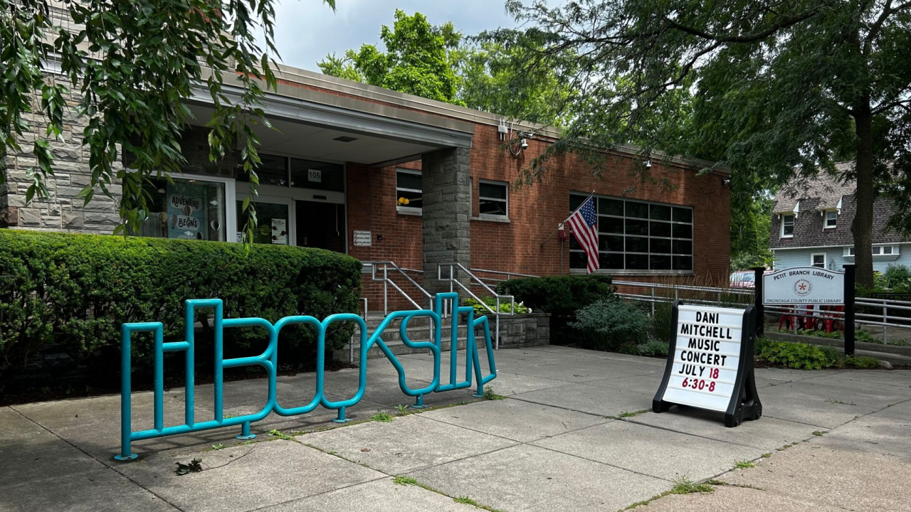 A brick building with greenery out front, in the foreground is a blue metal sculpture spelling out "Books"