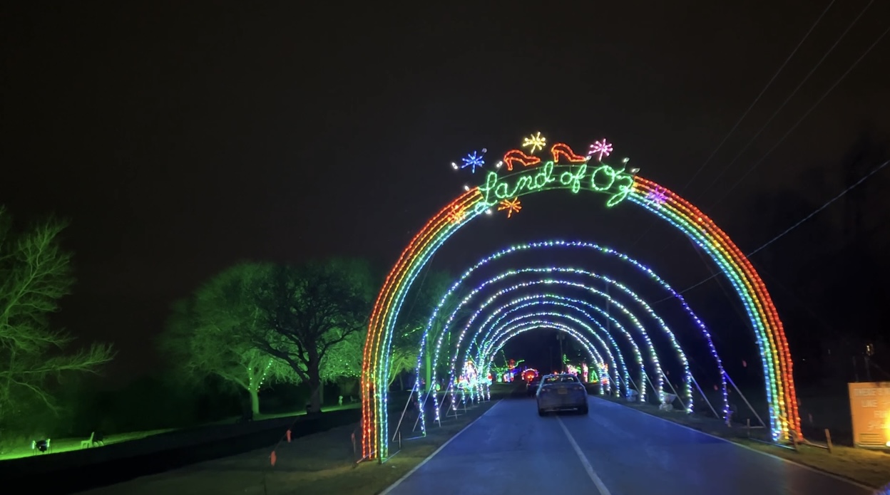 Rainbow light arch that says "Land of Oz," with cars driving through.