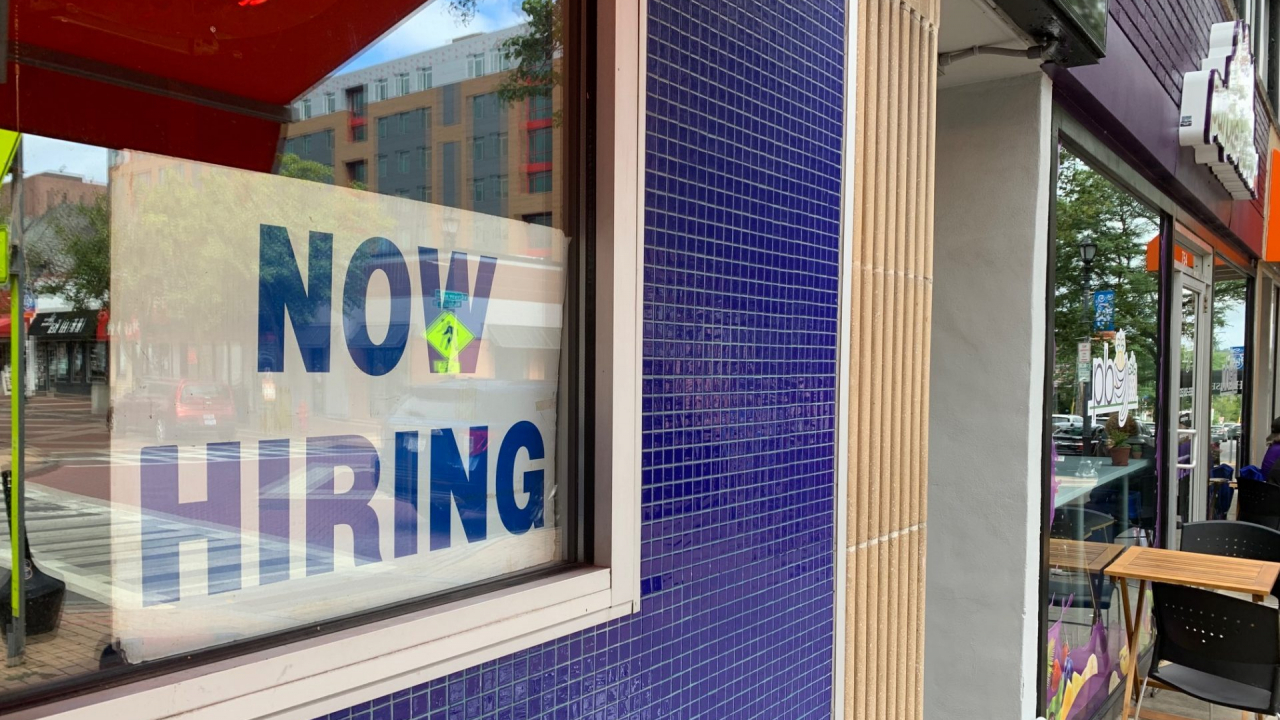 A Now Hiring sign is posted in the window of a local business.