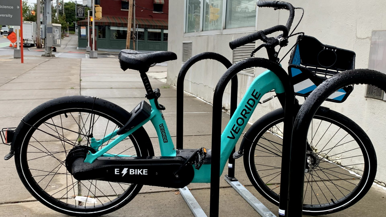 A mint green bike with the works VEORIDE sits locked up to a bike rack