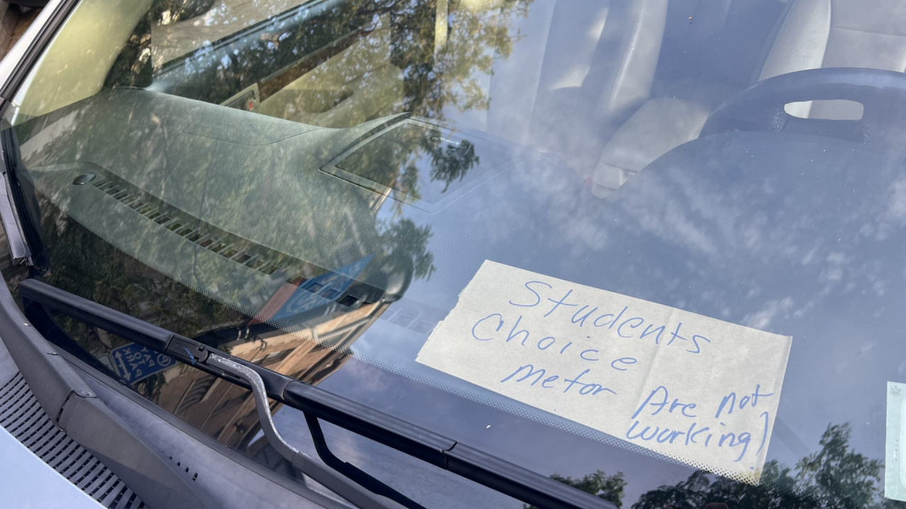 A sign that reads "student's choice meter are not working" on the dashboard of a car.
