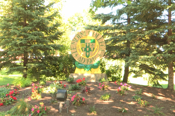 Picture of a Le Moyne College sign amongst trees and flowers at one of the entrances to the school.