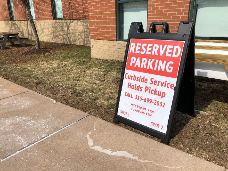 A red and white folding sign that reads "Reserved Parking: Curbside Service Holds Pickup" is placed on a strip of grass in front of a parking space.