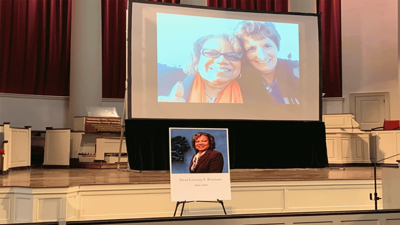 A photo of two women is projected onto a white screen and a smaller billboard featuring late Lorraine Branham is situated in front.