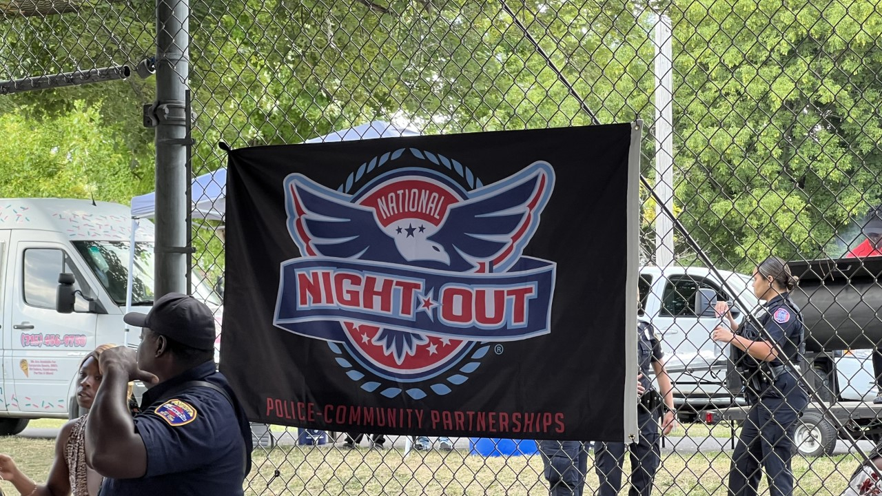 The National Night Out flyer is displayed behind a police officer and community member.