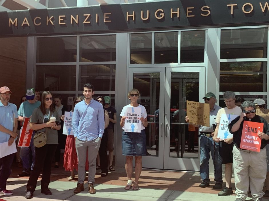 Protesters stand outside of Mackenzie Tower with signs.