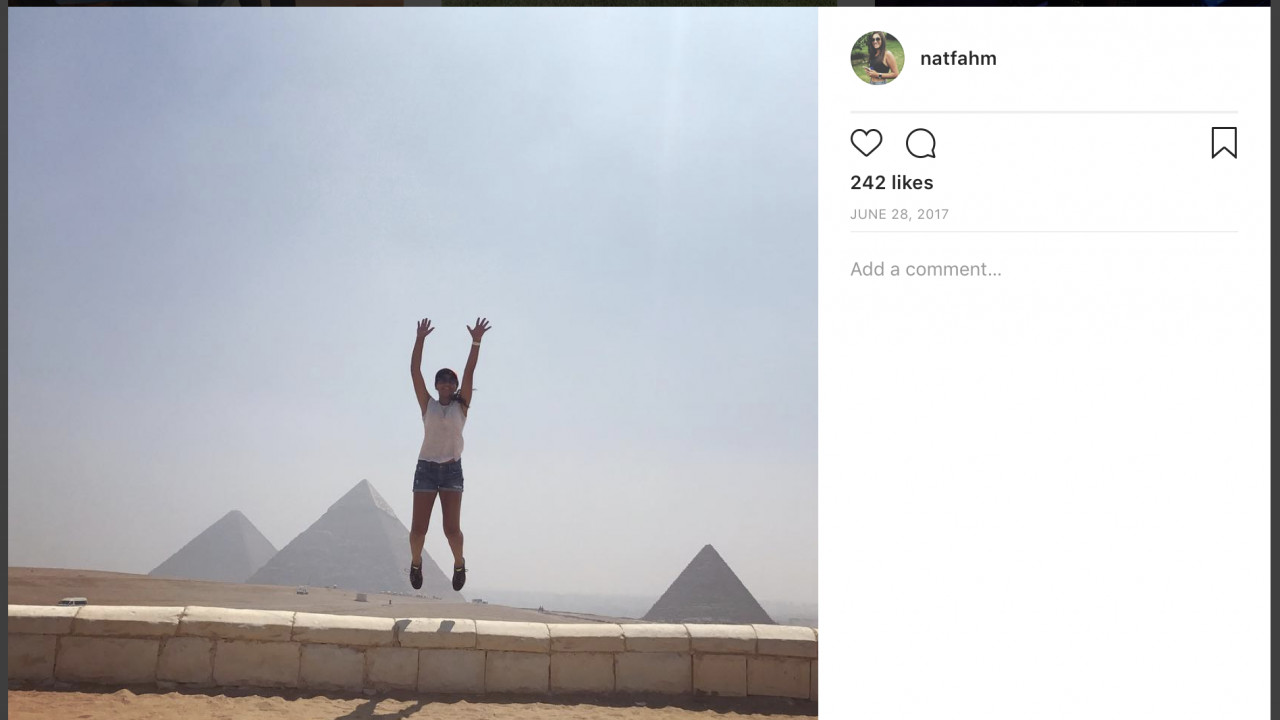 A screenshot of an instagram post that show a girl jumping in front of the great pyramids of giza.