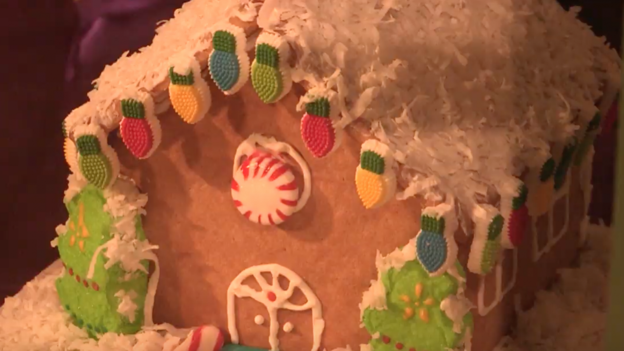 A gingerbread house with colored candy lights, a white icing roof, and green trees