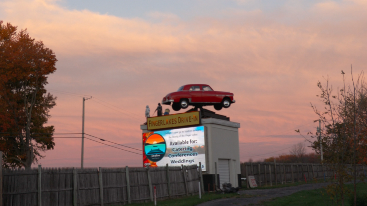 Sign that reads "Fingerlake Drive-In Movie Theatre" with vintage car on top of the sign.