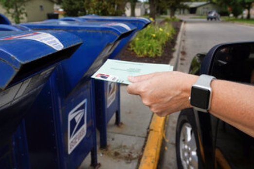 Person dropping their absentee ballot into a mail box.