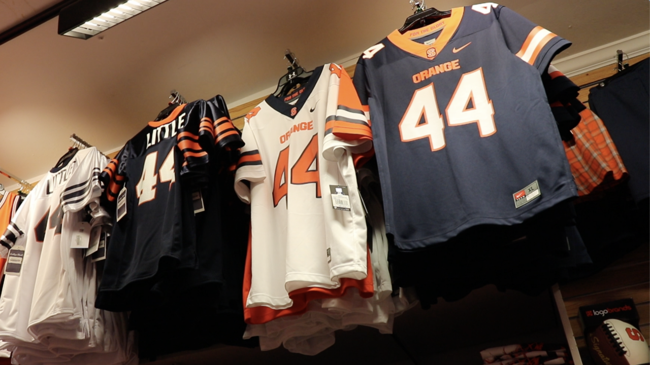 Four rows of Floyd Little jerseys hang on a wall. The jersey colors are white, navy, white and navy from left to right all with the number 44 on them.