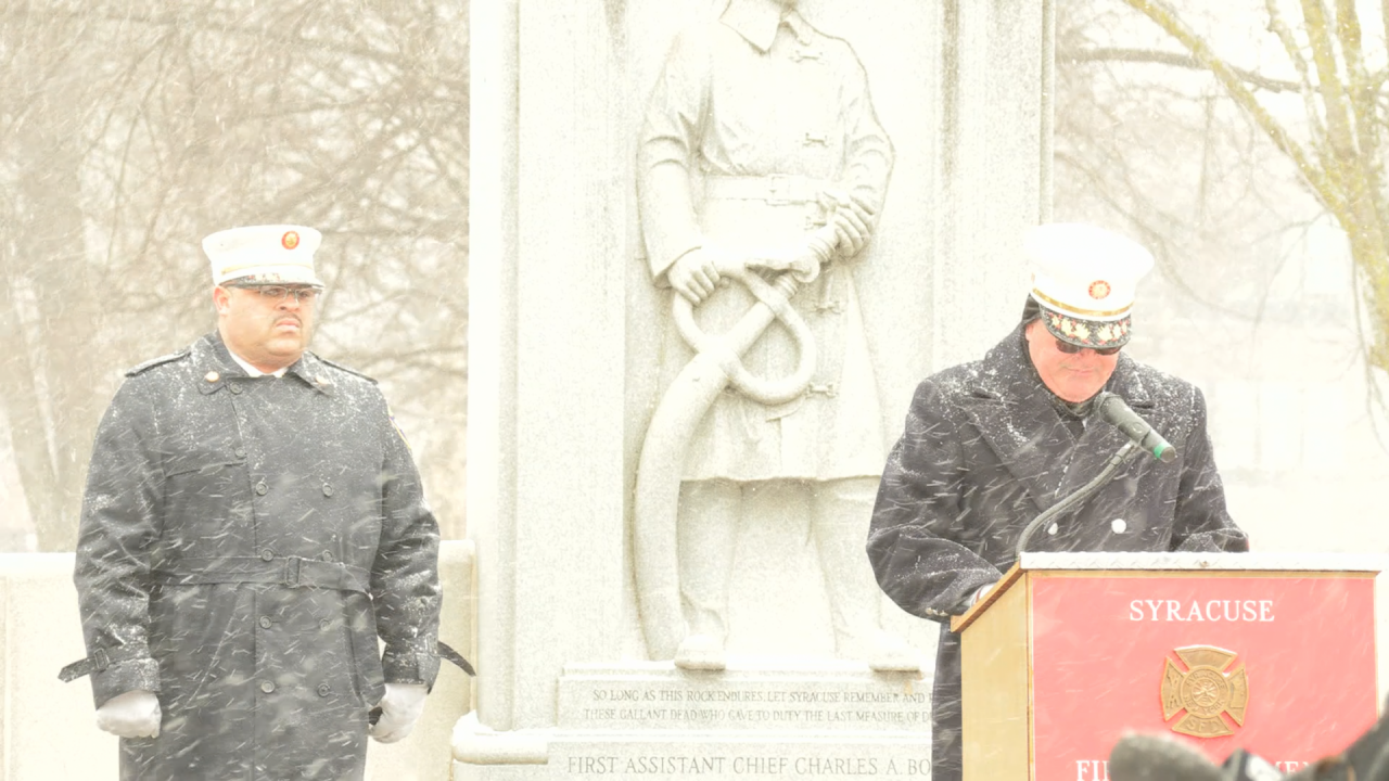 Two firefighters stand in front of a statue in the snow.
