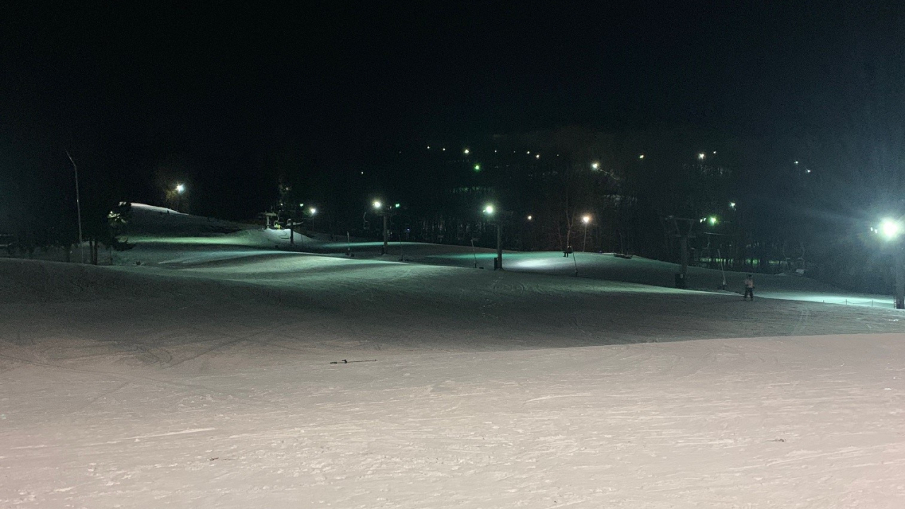 Snow on a ski slope with ski lights for night skiing in the distance.