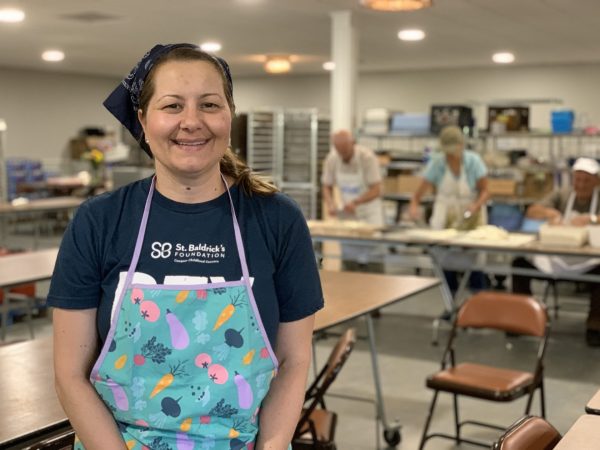 Woman wearing apron standing in front of church members preparing for Greek Food Fest