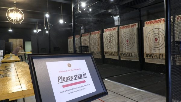 A sign welcomes patrons into Far Shot Syracuse with wooden boards set up in the background for axe throwing