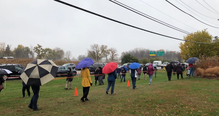 Voters with umbrellas stand outside waiting to cast their ballots on a rainy afternoon in Dewitt.