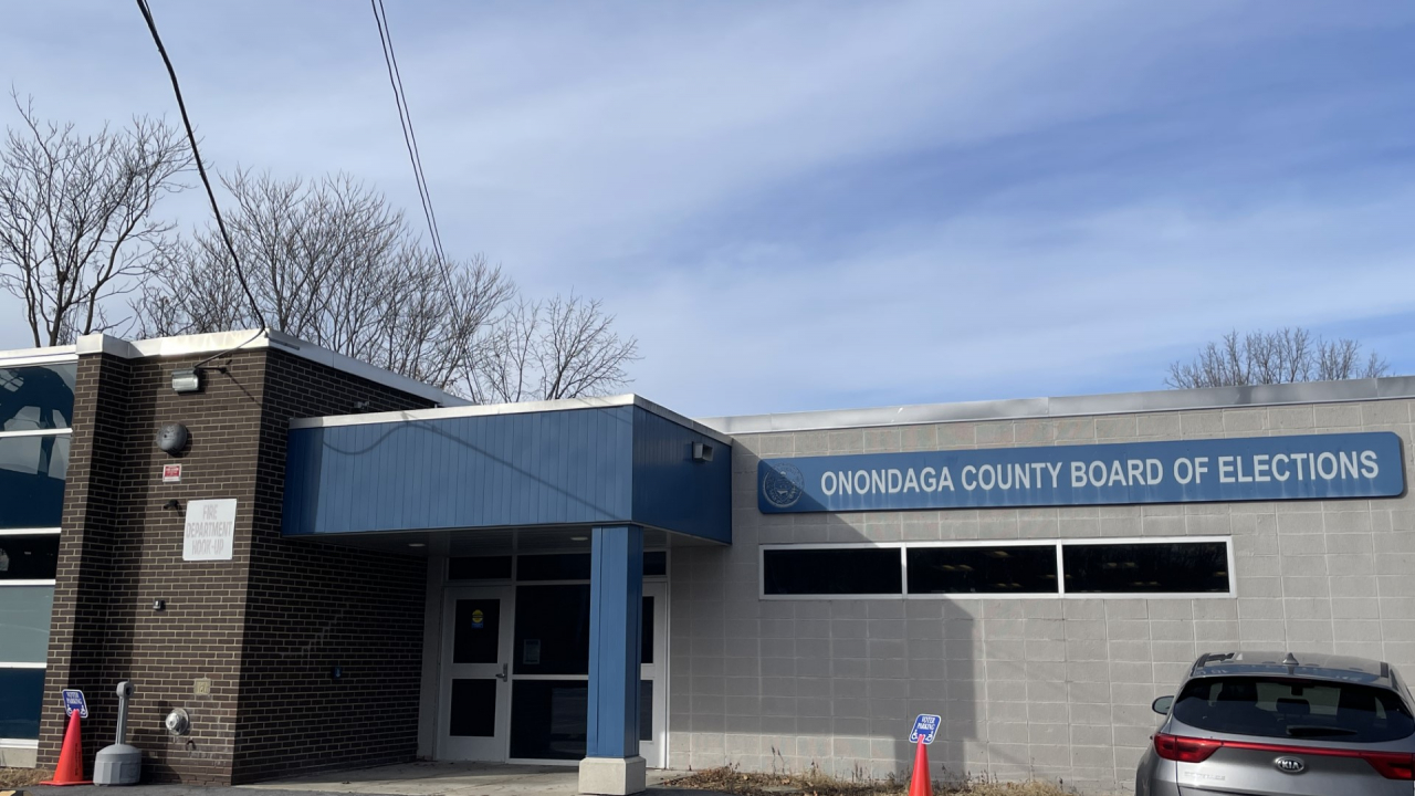Gray building with Onondaga County Board of Elections written in white font in front of a blue background.