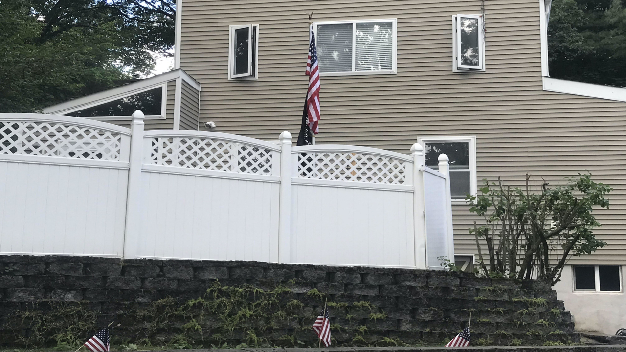 An American flag hanging on a flagpole behind a cleaned white fence.