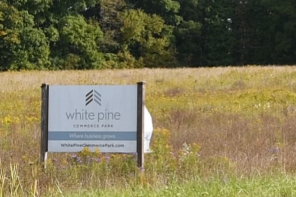 An image of a field and trees with a sign reading "White Pine Commerce Park" in the foreground.