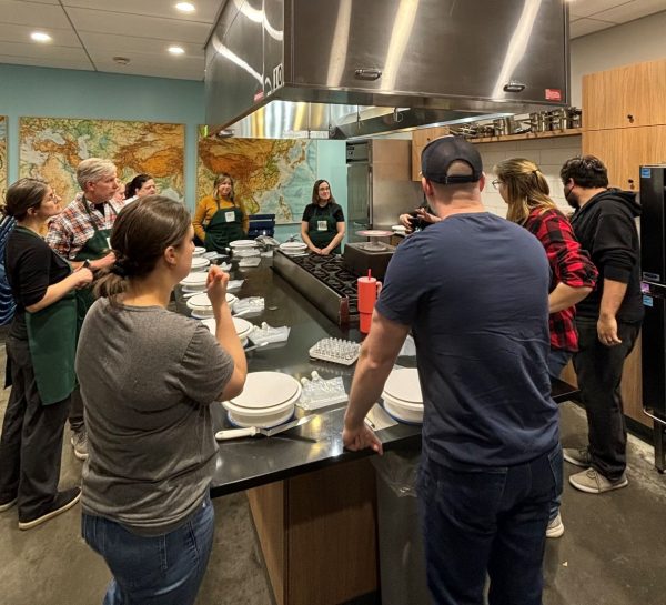 People standing around a kitchen table in a cake decorating class.