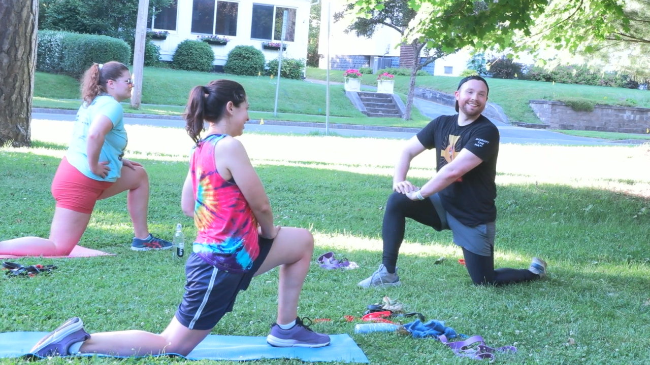 man in black shit and pants kneels in a lunge with two women in colorful clothing mimicing the motion.