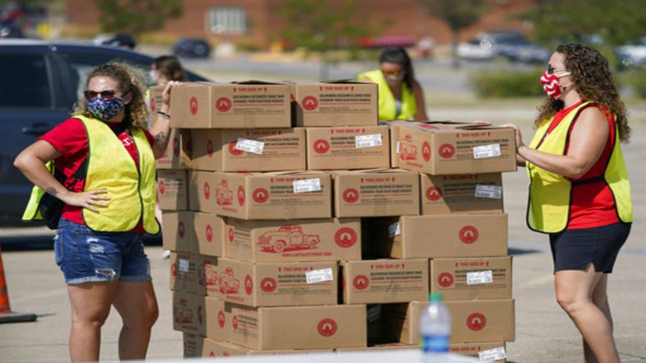 Volunteers stand next to piles of boxes at a food drive.