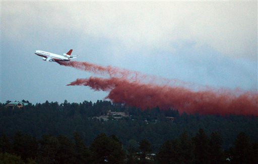A plane drops material over a forest to help put out a fire