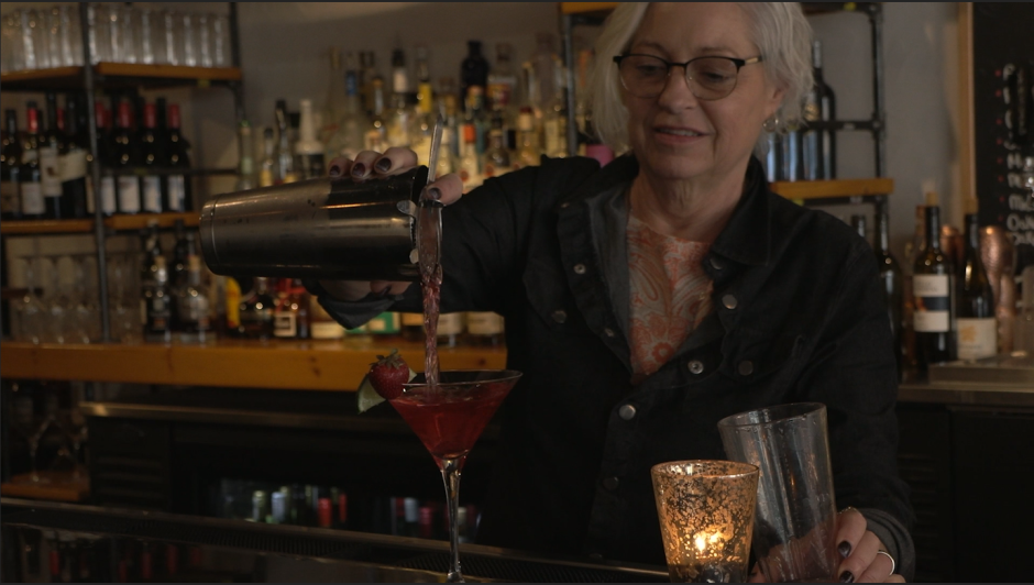 A bartender pours a cosmo into a martini glass at The Tasting Room